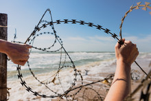 Hands Open Barbed Wire Outdoors At Beach.