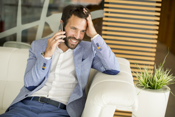 Wall Mural - Happy young businessman sitting in office and using mobile phone