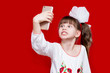 © Svetlana - Little girl with crazy face hold telephone and take picture on red background. Communication concept