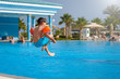 Caucasian child in floating sleeves jumping into swimming pool at resort.