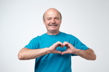 Old Caucasian Man In Blue T-shirt Making Out Of Hands Heart.