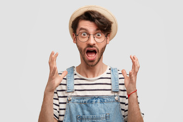 Wall Mural - Omg, it`s terrible! Emotive male agricultural worker gestures angrily, opens mouth widely and stares with bugged eyes, being discontent with seasonal harvest, wears casual countryside outfit