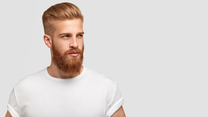 Serious thoughtful male with ginger beard, dressed casually, focused somewhere, isolated over white background with free space on right for your advertising content. Pensive red haired hipster