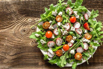 Wall Mural - Healthy diet. Vegetable Fresh salad with arugula leaves, tomato, radish and seeds. Dietary appetizer or lunch on plate, vegetarian food concept.