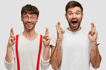 Wall Mural - Happy male students anticipate results of exam, cross fingers as believe in good luck, stand closely, being very emotive, isolated over white background. People, body language and wish concept