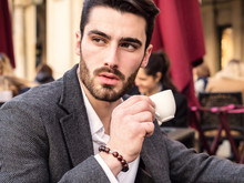 Handsome Young Man Drinking Espresso Coffee, Wearing Elegant Coat Posing At Table Outside On Elegant Urban Background In Turin, Italy