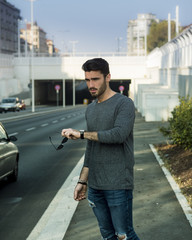 Wall Mural - Attractive young bearded man portrait in urban environment, in a street, looking at cars