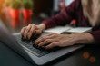 © eskstock - Typing on laptop close up. Young businesswoman sitting at table in coffee shop, look at your notebook screen and ponder business strategy. Girl taking notes in notebook. On table laptop and notebook.
