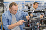 Fototapeta  - mature man repairing bike wheel in his own store