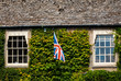 Medieval Cotswold stone cottage with British flag between windows in the village of Bibury, England