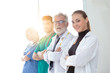 © thbangkok - Confident female doctor looking at camera and smiling while her colleagues standing in a row behind her. A team of experienced highly qualified doctors.