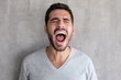 © Damir Khabirov - Closeup portrait of screaming with closed eyes crazy young man, standing against gray textured wall
