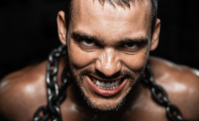 Portrait of muscular slave in chains on black backround, the prisoner