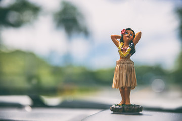 Hawaii road trip - car hula dancer doll dancing on the dashboard in front of the ocean. Tourism and travel freedom concept.