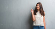 © Krakenimages.com - Young brunette woman over grunge grey wall surprised with an idea or question pointing finger with happy face, number one