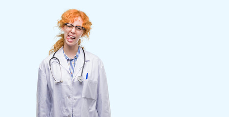 Poster - Young redhead woman wearing doctor uniform sticking tongue out happy with funny expression. Emotion concept.