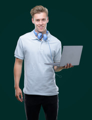 Sticker - Young handsome blond man using a laptop with a happy face standing and smiling with a confident smile showing teeth