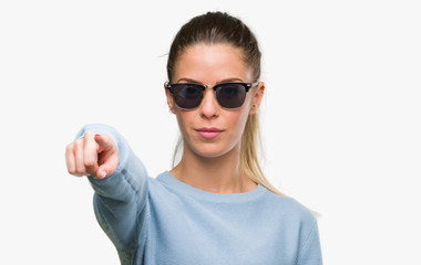 Sticker - Beautiful young woman wearing sunglasses and ponytail pointing with finger to the camera and to you, hand sign, positive and confident gesture from the front