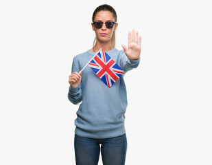 Poster - Beautiful young woman holding UK flag with open hand doing stop sign with serious and confident expression, defense gesture