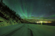 Northern lights Aurora Borealis in the night above a arctic snowy road on a fjord