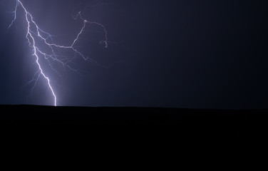 Single lightning strike in nature in a field with colours of white and blue electricity and no buildings in the landscape image