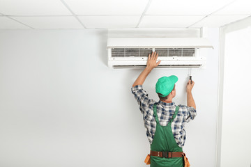 Male technician fixing modern air conditioner indoors