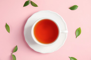 Cup of delicious tea with green leaves on color background, top view