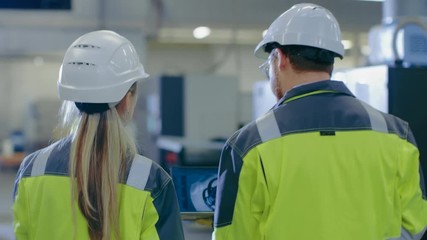 Poster - Following Shot of Male and Female Mechanical Engineers Talking, while  Walking Through Industrial Factory, Male Holds Laptop With Engine Project. 