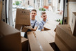 Two young handsome smiling movers wearing uniforms are unloading the van full of boxes. House move, mover service.