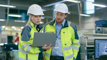Poster - Male and Female Industrial Engineers Wearing safety,  Work on a Factory, They Discuss Project while Using Laptop.In the Background Industrial Facility.