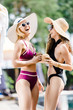 © LIGHTFIELD STUDIOS - attractive girls in swimsuits laughing and holding coconut cocktails near swimming pool