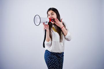 Portrait of a young woman in blue trousers and white blouse posing with megaphone in the studio.