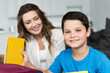 © LIGHTFIELD STUDIOS - selective focus of smiling boy with book and mother behind at home