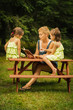 © superelaks - beautiful mother and two adorable daughters in dresses posing on a picnic table in a summer forest