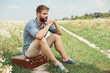 © LIGHTFIELD STUDIOS - pensive stylish man sitting on retro suitcase in field with wild flowers