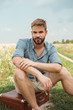 © LIGHTFIELD STUDIOS - young stylish man sitting on retro suitcase in field with wild flowers