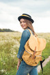 © LIGHTFIELD STUDIOS - portrait of smiling attractive woman in hat with yellow backpack standing in field