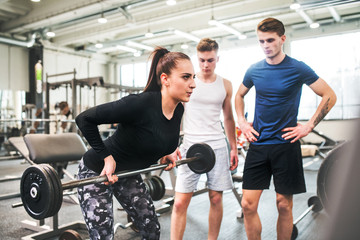 Wall Mural - Female personal trainer showing young men how to lift barbell.