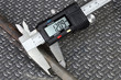 © Valentin - Measurement of a threaded steel rod with digital caliper over corrugated metal background
