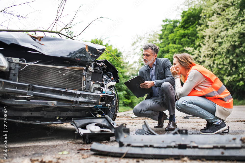 An insurance agent and a woman driver looking at the car on the road after an accident. - obrazy, fototapety, plakaty 