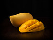 Side view image of close up appetizing yellow mango fruit and mango cubes on wooden table on black backbround