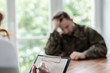 © Photographee.eu - Close-up of a hand writing on a piece of paper with a depressed soldier in the blurred background