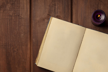 Wall Mural - An old book with a candle on a dark rustic background with copy space