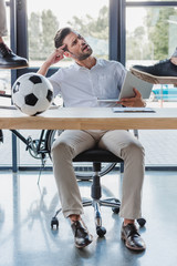 Wall Mural - cropped shot of men kicking soccer ball on table while angry colleague using laptop in office