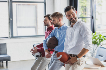 Wall Mural - happy young businessmen holding balls and looking away in office