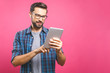 © denis_vermenko - Happy young man in plaid shirt standing and using tablet over pink background