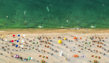 Aerial View Of A Beach With Colorful Umbrellas, People Swimming In The Sea, Sunny Day. Drone Landscape From Above