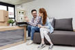 © pucko_ns - Young couple in new home with notebook sitting on sofa and planning with unpacked boxes in background