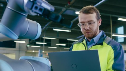 Poster - Handheld Shot At the Factory: Automation Engineer Uses Laptop for Programming and Testing Robotic Arm. New Era in Automatic Manufacturing Industry.