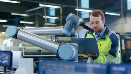 Poster - At the Factory: Automation Engineer Uses Laptop for Programming Robotic Arm. New Era in Automatic Manufacturing Industry. Shot on RED EPIC-W 8K Helium Cinema Camera.